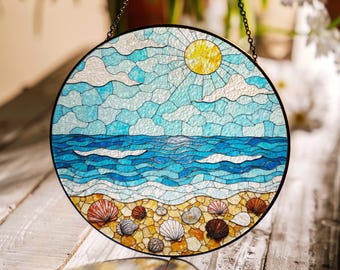 Puede incluir: Una ventana redonda de vitral colgada de una cadena. La ventana representa una escena de playa con un océano azul, nubes blancas, un sol amarillo y conchas en la arena.