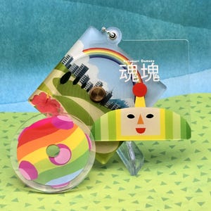 Puede incluir: Un conjunto de colgantes acrílicos coloridos con un arcoíris, un paisaje urbano y un personaje con un sombrero amarillo y verde. Los colgantes tienen un fondo transparente y están unidos a un llavero plateado. El texto "魂魄" es visible.