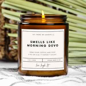 Könnte beinhalten: Eine braune Glaskerze mit einem weißen Etikett, auf dem "Let There Be Laughs" und "Smells Like Morning Devo" steht. Das Etikett enthält auch den Text "Grab your coffee and post a pic or else it doesn't count." und "9 oz / 2550". Die Kerze ist vegan und wurde in den USA hergestellt.