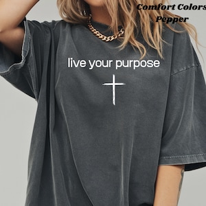 Puede incluir: Camiseta gris oscuro Comfort Colors con el texto "live your purpose" y una cruz blanca. La camiseta tiene mangas cortas y un corte holgado. El texto "Comfort Colors Pepper" está impreso en la parte superior.