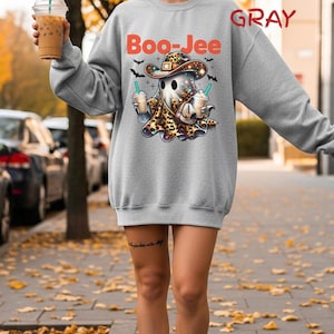 May include: A sport gray crewneck sweatshirt featuring a graphic of a ghost wearing a leopard print cowboy hat and holding two iced coffee drinks. The text "Boo-Jee" is printed in orange above the ghost, and "SPORT GRAY" is printed in red.