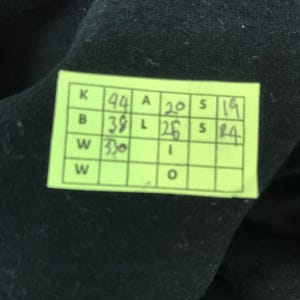 May include: A close-up of a neon green tag with black text and numbers. The tag is rectangular and has multiple boxes with numbers and letters. The background is black.