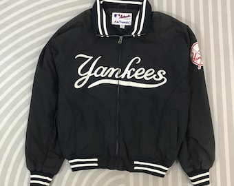 May include: Black Yankees baseball jacket with white "Yankees" script across the chest. The jacket has a white collar and cuffs with navy blue stripes. A Yankees logo patch is on the right sleeve. The jacket is made by Majestic.