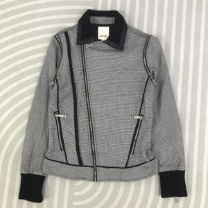 Könnte beinhalten: Schwarz-weiß karierte Jacke mit schwarzem Kragen und Manschetten. Die Jacke hat einen diagonalen Reißverschluss und zwei Reißverschlusstaschen. Der Markenname "DIESEL" ist auf einem kleinen Etikett am Kragen zu sehen.