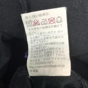 May include: A white clothing tag with Japanese text and care symbols. The tag includes washing instructions, ironing instructions, and drying instructions. The tag also includes the manufacturer's contact information.