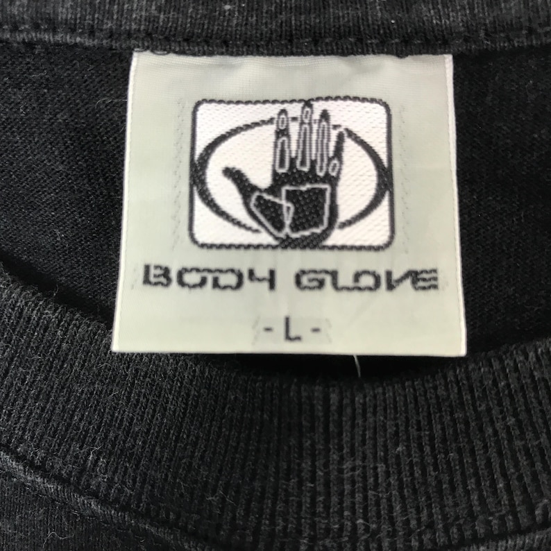 May include: Close-up of a black t-shirt tag with the "BODY GLOVE" logo in white. The logo features a hand inside an oval. The tag also has the size "-L-" printed in black.