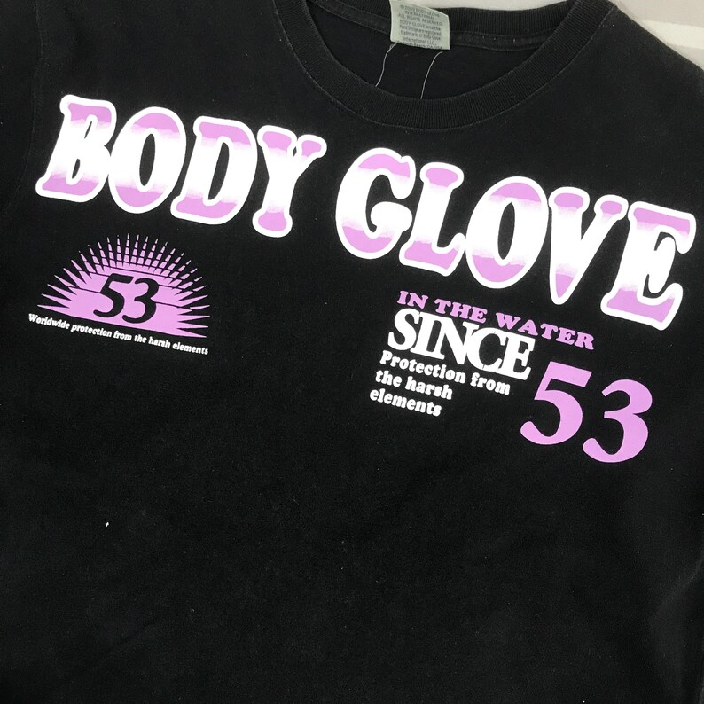May include: Black t-shirt with the text "BODY GLOVE" in white and pink lettering. The shirt also features the number "53" and the phrase "Worldwide protection from the harsh elements."