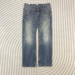 May include: Faded blue denim jeans with a straight leg cut. The jeans have a button fly, classic five-pocket design, and subtle distressing. The denim has a worn-in appearance with light fading and whiskering.