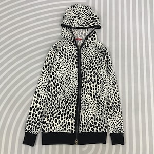 May include: A black and white zip-up hoodie with a matching hood. The hoodie features a spotted pattern and a black zipper. The cuffs and waistband are solid black. The hoodie is made of a soft material.