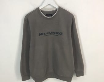 May include: A gray sweatshirt with the text "Mr. Junko Junko Koshino" printed across the chest. The sweatshirt has a crew neck with a white collar and long sleeves. It is hanging on a white hanger.