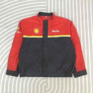 May include: Red and gray Shell Helix racing jacket. The jacket has a stand-up collar, a zipper closure, and multiple logos, including the Shell logo and the word "HELIX". The sleeves are red, and the body is gray.