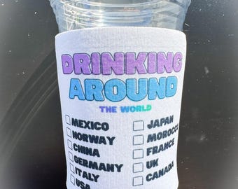 May include: A clear plastic cup with a white drink sleeve. The sleeve has the words "DRINKING AROUND THE WORLD" in purple and blue. Checkboxes list countries like Mexico, Japan, and Canada.