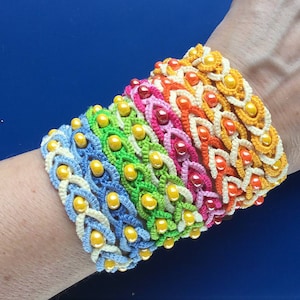 Może przedstawiać: Stos kolorowych bransoletek na szydełku z żółtymi koralikami. Bransoletki są w odcieniach niebieskiego, zielonego, żółtego, pomarańczowego, czerwonego i różowego.