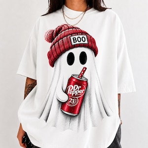 Può includere: Una t-shirt bianca con la grafica di un fantasma che indossa un berretto di lana rosso con una toppa con la scritta BOO. Il fantasma tiene in mano una lattina di bibita rossa con l'etichetta Dr Pepper e una cannuccia. Il disegno è centrato.