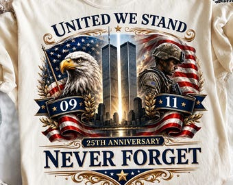 May include: A cream-colored t-shirt featuring a graphic with the text UNITED WE STAND, 09 11, 25TH ANNIVERSARY, and NEVER FORGET. The design includes a bald eagle, the Twin Towers, a soldier in uniform, and American flags with gold accents.