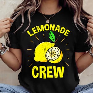 May include: Black t-shirt with a yellow graphic of a lemon and the words "LEMONADE CREW". The design includes a whole lemon and a lemon slice with a green leaf. The text and lemon design have a distressed, vintage look.