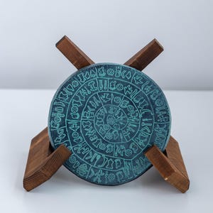 Disco de terracota antiguo patinado verde Reproducción griega Disco de Festos Artefacto cultural griego Caja de museo Disco minoico Monumento con letras