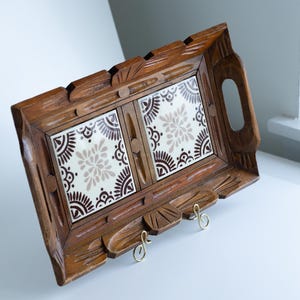 Peut inclure: Un porte-clés en bois avec un motif de carreaux floraux décoratifs. Le porte-clés est rectangulaire avec un cadre en bois sculpté et deux crochets en laiton. Les carreaux sont blancs avec un motif floral marron et beige. Le porte-clés a une poignée sur le côté.