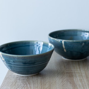 Może przedstawiać: Dwie niebieskie ceramiczne miski o teksturowanym, żłobkowanym wzorze. Miski mają błyszczące wykończenie i stoją na drewnianej powierzchni. Miski są różnej wielkości, z mniejszą miską na pierwszym planie.