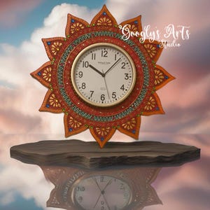 May include: A round, orange and red clock with a white face and black hands. The clock is decorated with intricate details and is surrounded by a mandala-like design. The clock is reflected in a pool of water below.
