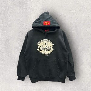 May include: Black hooded sweatshirt with a cream soda logo featuring a skull and crossbones. The logo reads "Too fast to live, too young to die" and "Cream Soda" with the text "Trade Mark 1992" underneath.