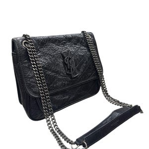 May include: A black crinkled leather shoulder bag featuring a prominent YSL logo on the front flap. The bag includes a dark metal chain strap with a leather shoulder pad. The text Saint Laurent Paris is embossed on the leather shoulder pad.