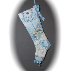 Könnte beinhalten: Ein blauer und weißer Patchwork-Weihnachtsstrumpf mit einem Vogelmotiv und blauen Knöpfen. Der Strumpf ist mit Spitze und einem blauen Band verziert.