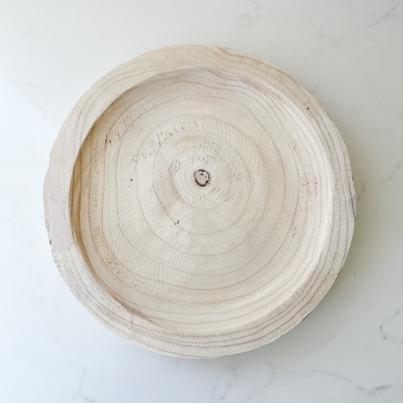 May include: A round wooden tray with a natural wood finish and visible wood grain. The tray has a slightly raised edge and a smooth surface.