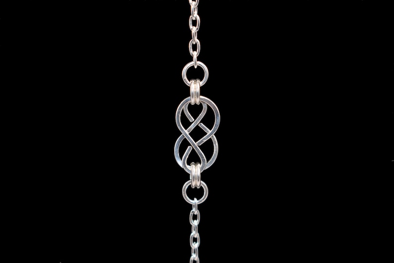 May include: A silver chain necklace with a silver infinity knot pendant.