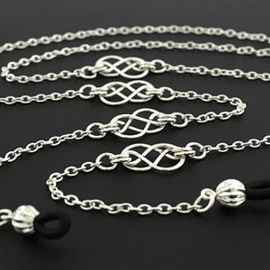 May include: Silver-toned eyeglass chain with a delicate chain design. The chain features Celtic knot accents and rubber loops for attaching to glasses. The chain is approximately 30 inches long.