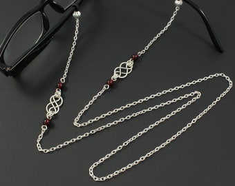 Könnte beinhalten: Silberne Brillenkette mit roten Perlen und einem silbernen Unendlichkeits-Symbol-Anhänger. Die Kette ist lang genug, um sie über den Kopf zu tragen.