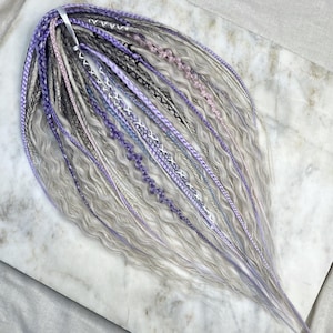 May include: A set of synthetic hair extensions in shades of gray, lavender, and light pink. The hair is wavy and has a natural look.