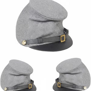 May include: A gray kepi hat with a black brim and a leather strap. The hat has a gold buckle and a gold button on the side. The hat is a historical military style.