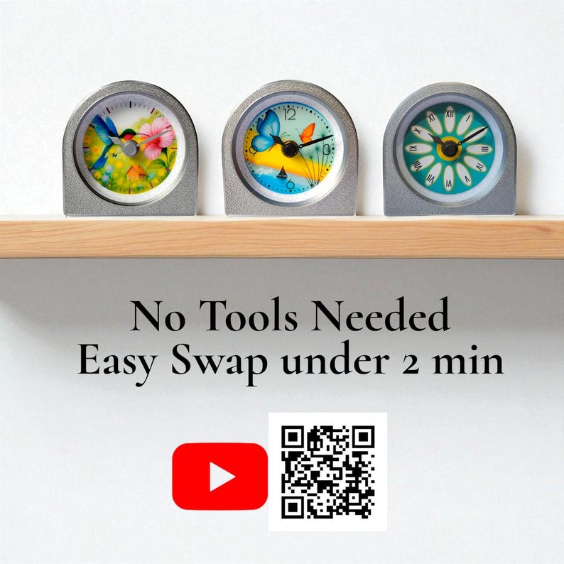Op de afbeelding: Drie kleine, zilverkleurige klokken met kleurrijke bloemen- en vlinderontwerpen op een houten plank. De wijzerplaten tonen een kolibrie, een vlinder en een madeliefje. De tekst "No Tools Needed Easy Swap under 2 min" staat eronder.