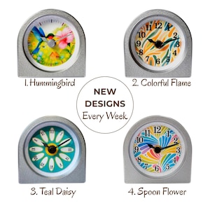 May include: Four small, silver-colored clocks with different face designs. The designs include a hummingbird, colorful flame, teal daisy, and spoon flower. The text "NEW DESIGNS Every Week" is also present.