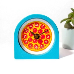 May include: A novelty pizza-themed desk clock with a bright blue frame. The clock face features a pizza design with pepperoni and a brown clock hand. The numbers are in a yellow font. The clock is a fun and unique decorative item.
