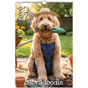 Op de afbeelding: Een wandkalender voor 2027 met een goudkleurige hond die een strooien hoed en een blauw spijker-schort draagt. De hond houdt een groen plastic tuinschepje in zijn bek. De achtergrond toont een tuin met bloemen in potten en aarde.