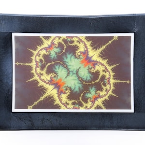 May include: A black framed picture with a colorful fractal design in the center. The design is a mix of yellow, green, orange, and red colors.