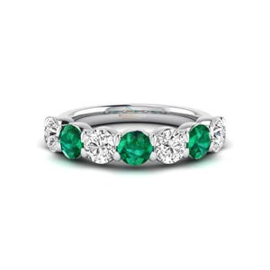 May include: A silver ring featuring a series of alternating emerald and diamond gemstones. The ring showcases a row of vibrant green emeralds and sparkling white diamonds, set in a polished silver band. The gemstones are oval-cut and evenly spaced.