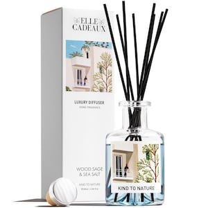 Puede incluir: Un difusor de vidrio transparente con cañas negras, una caja blanca y una tapa plateada. La caja y la botella presentan una ilustración en acuarela de un edificio. El texto en la caja dice "ELLE CADEAUX LUXURY DIFFUSER WOOD SAGE & SEA SALT KIND TO NATURE".
