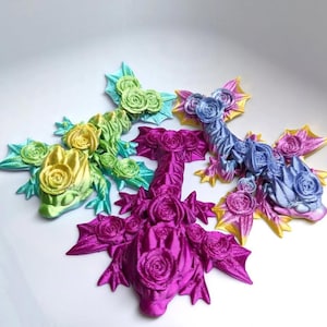 May include: Four decorative dragon figurines in shades of green, yellow, purple, and blue. Each dragon features rose-like details on its body and wings. The figurines are arranged on a white surface.