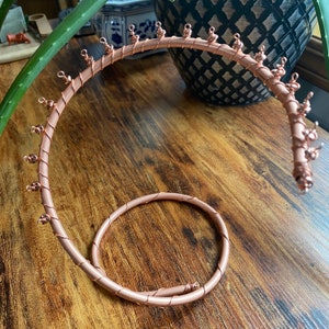 May include: A rose gold wire jewelry stand with multiple hooks for hanging earrings, necklaces, or bracelets. The stand is shaped like a spiral and has a circular base.