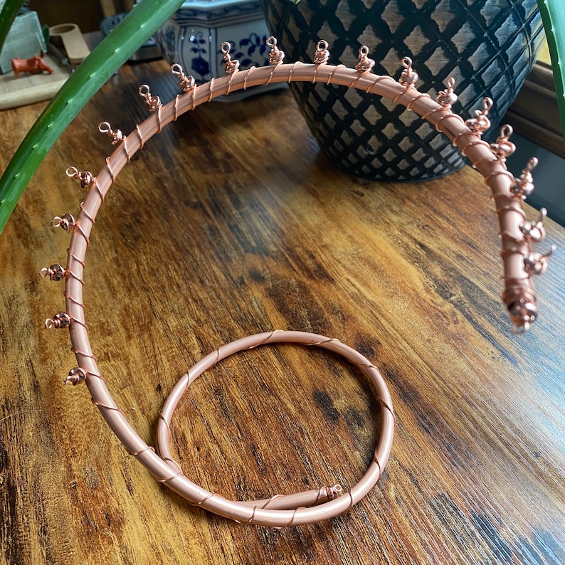 May include: A rose gold wire jewelry stand with multiple hooks for hanging earrings, necklaces, or bracelets. The stand is shaped like a spiral and has a circular base.
