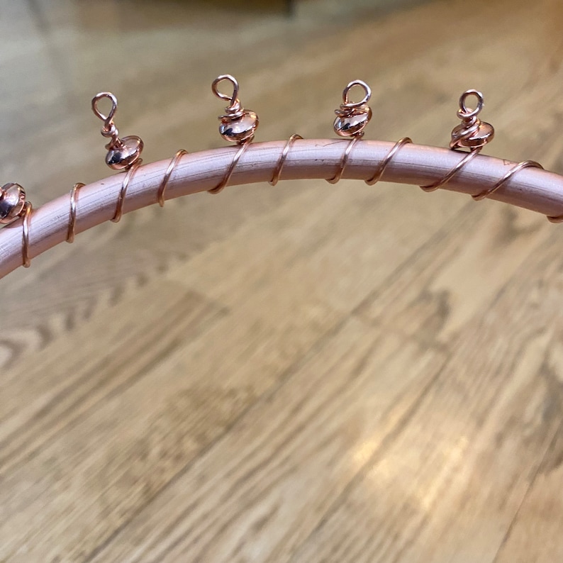 May include: A close-up of a rose gold wire headband with five rose gold beads attached. The beads have a loop at the top.