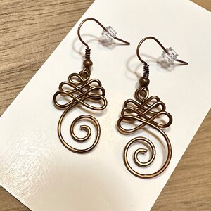 May include: A pair of bronze-coloured wire earrings with a swirling, knot-like design. The earrings have a simple hook fastening.