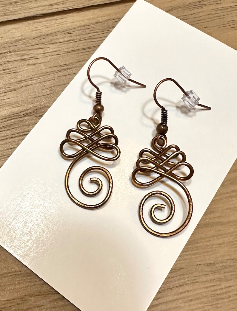 May include: A pair of bronze-coloured wire earrings with a swirling, knot-like design. The earrings have a simple hook fastening.