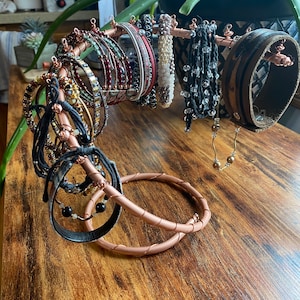 May include: A copper wire jewelry stand with a variety of bracelets and bangles. The stand is shaped like a twisted branch with a circular base. The bracelets are made of leather, beads, and metal.
