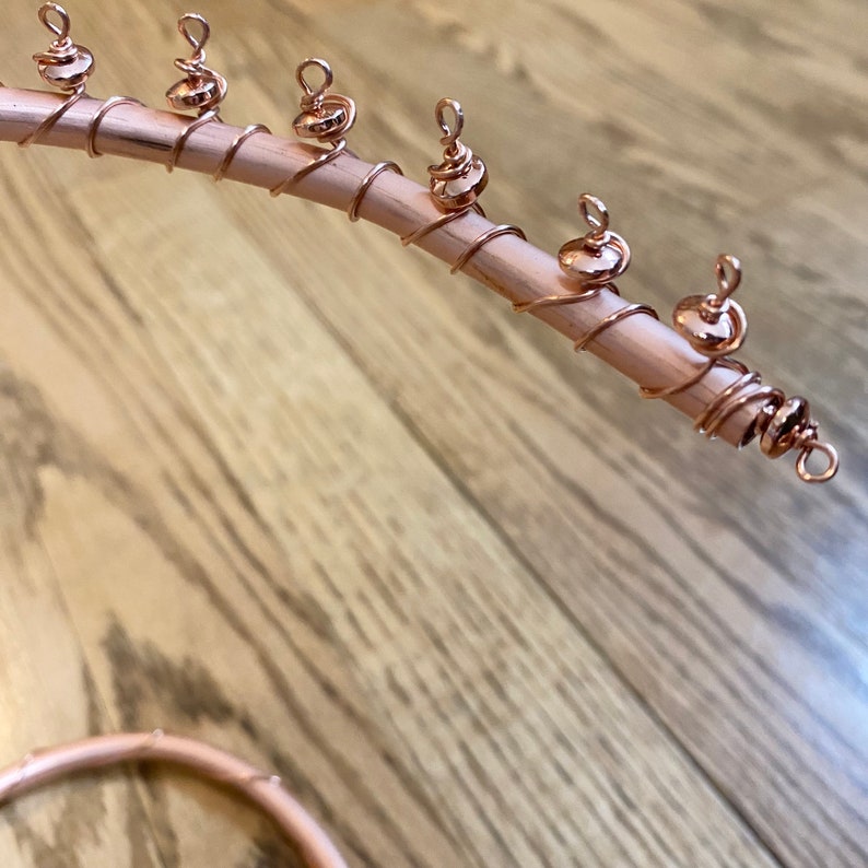 May include: A close-up of a rose gold wire wrapped hair stick with multiple rose gold beads attached. The hair stick is on a wooden surface.