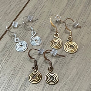 May include: A collection of spiral-shaped earrings in silver, gold, and copper tones. The earrings feature a coiled design and are displayed with clear earring backs. The hooks are visible, showcasing the different metal finishes.