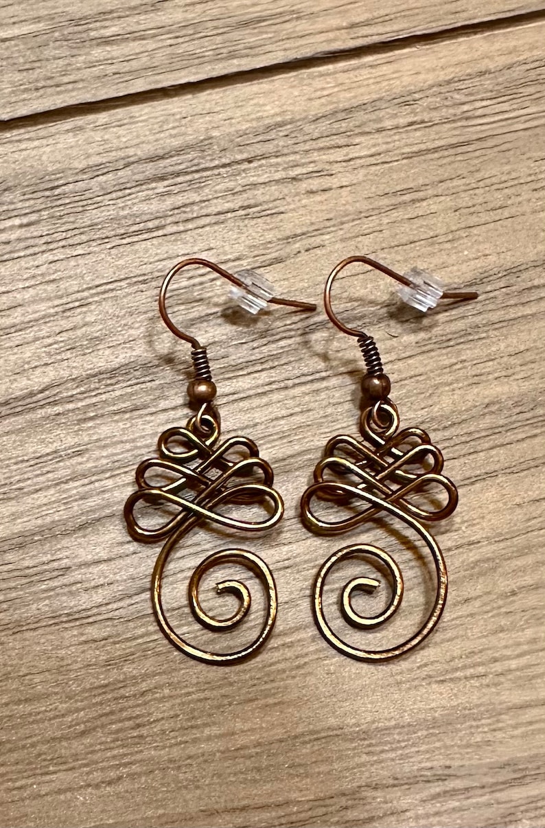 May include: A pair of gold-toned earrings with a delicate, intricate design. The earrings are made of wire and have a spiral shape at the bottom.